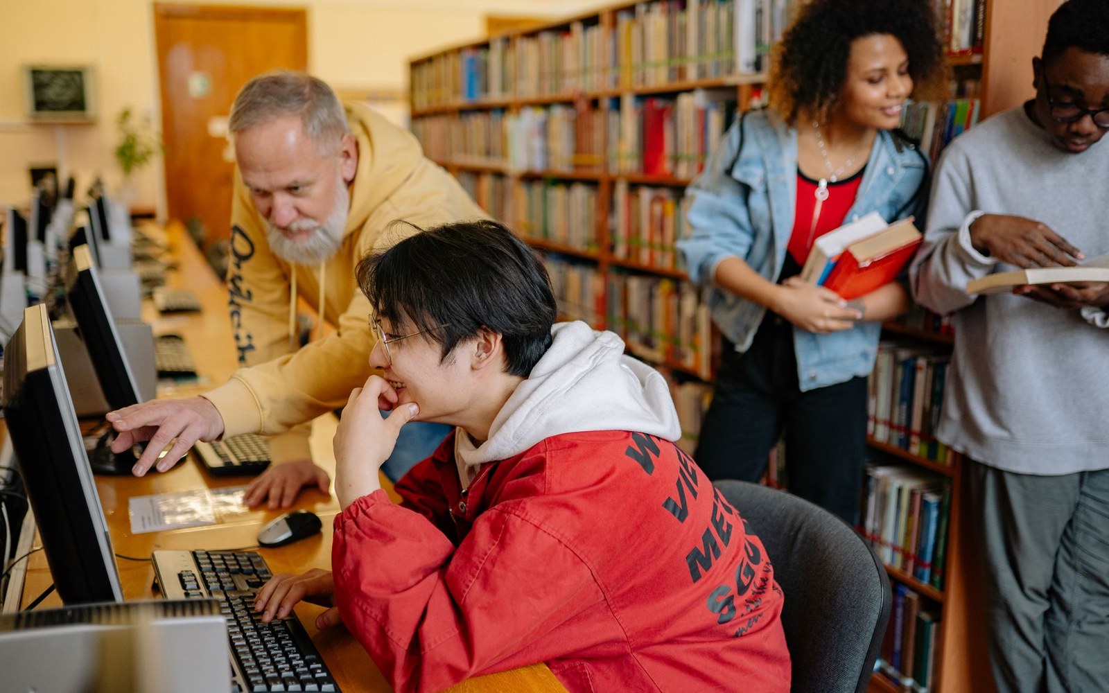 A student uses a library computer while a mentor points at the screen nearby