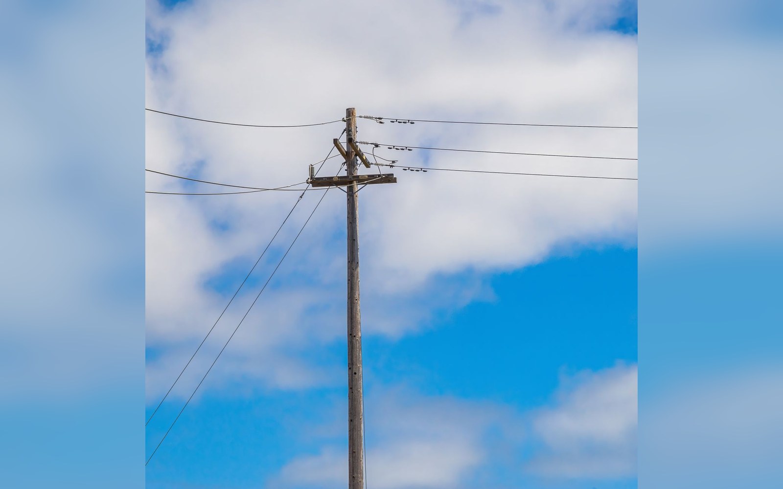 Wooden utility pole with power lines against a partly cloudy blue sky