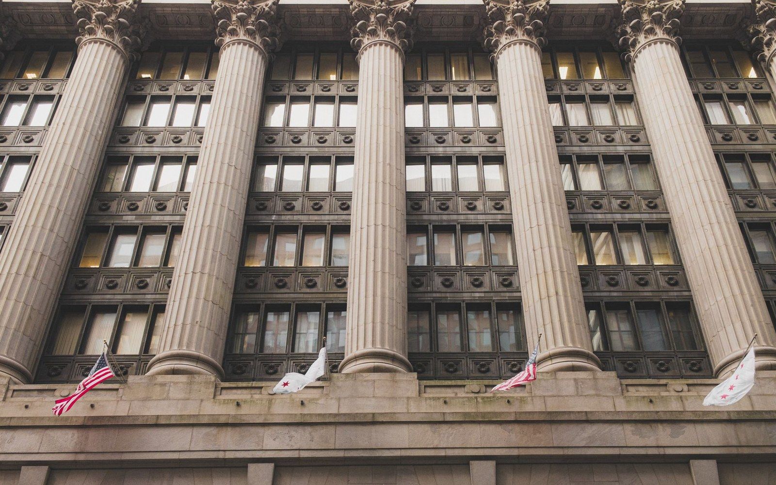 Corinthian columns line a stone building facade with American and Chicago flags below