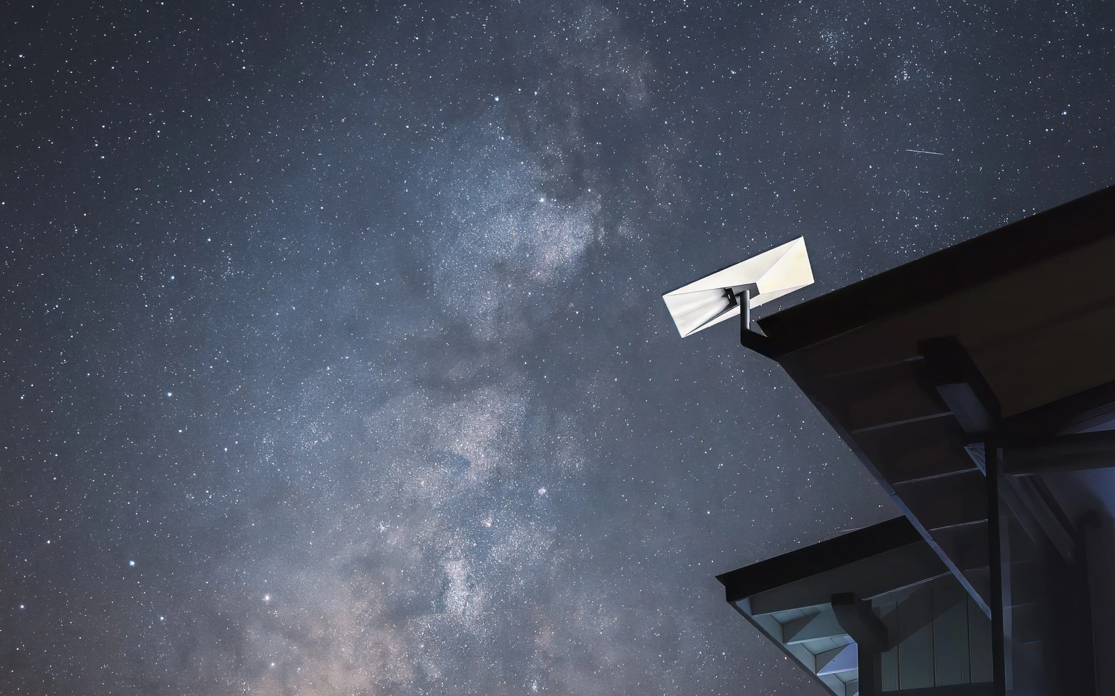A satellite dish mounted on a rooftop eave beneath a star-filled night sky