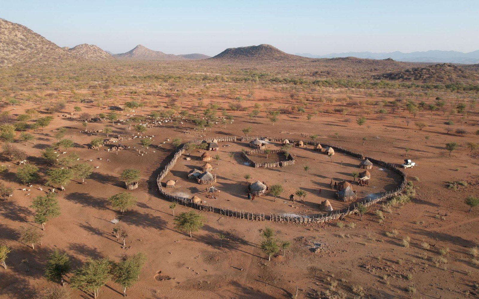 Aerial view of a circular fenced homestead with thatched huts in a semi-arid savanna