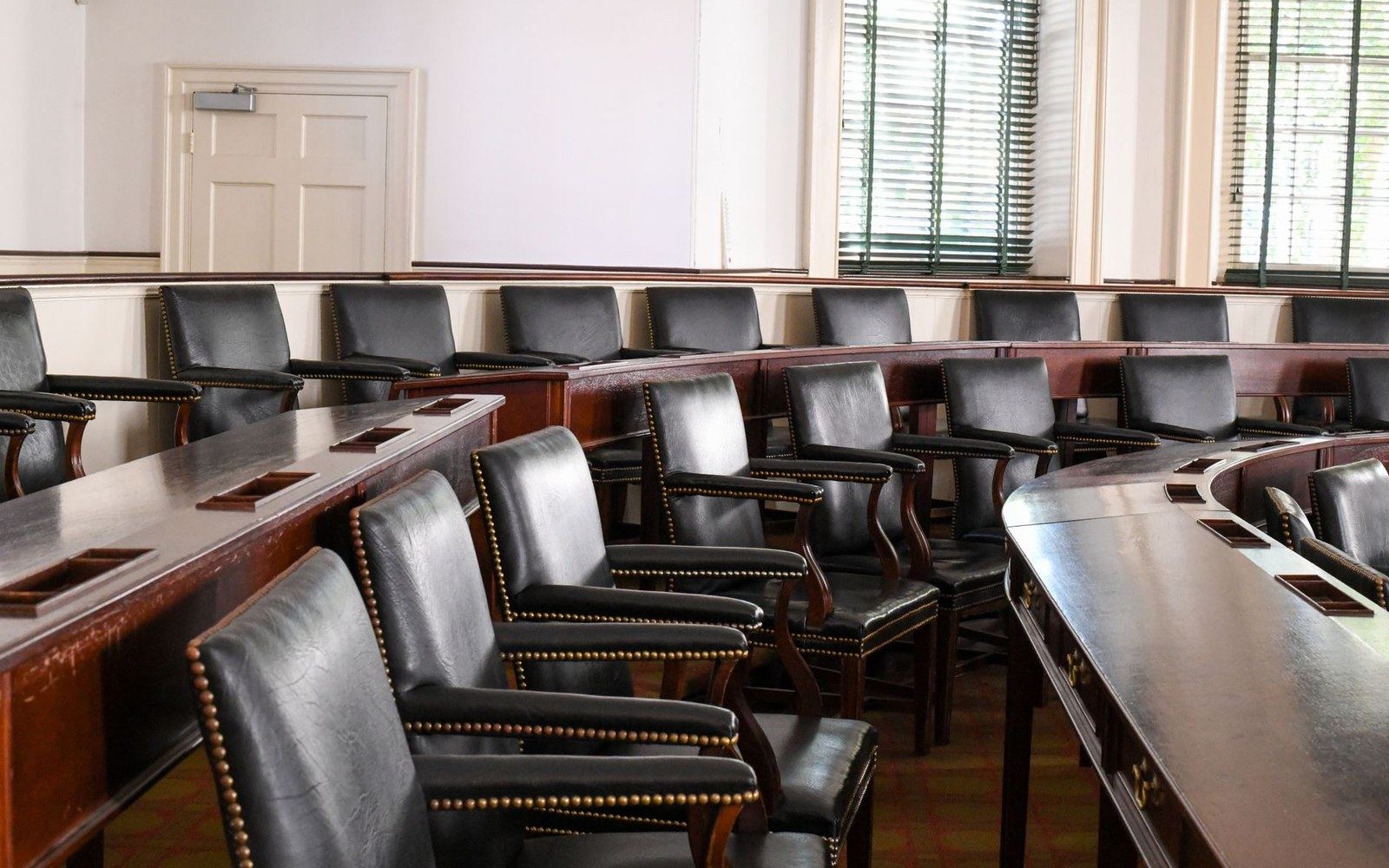 Empty leather chairs arranged in curved rows around wooden desks in a boardroom