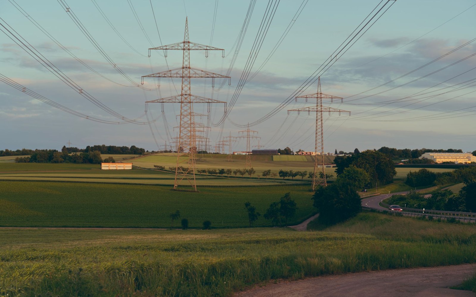 Transmission pylons and lines crossing farmland at dusk, a road running along the field edge